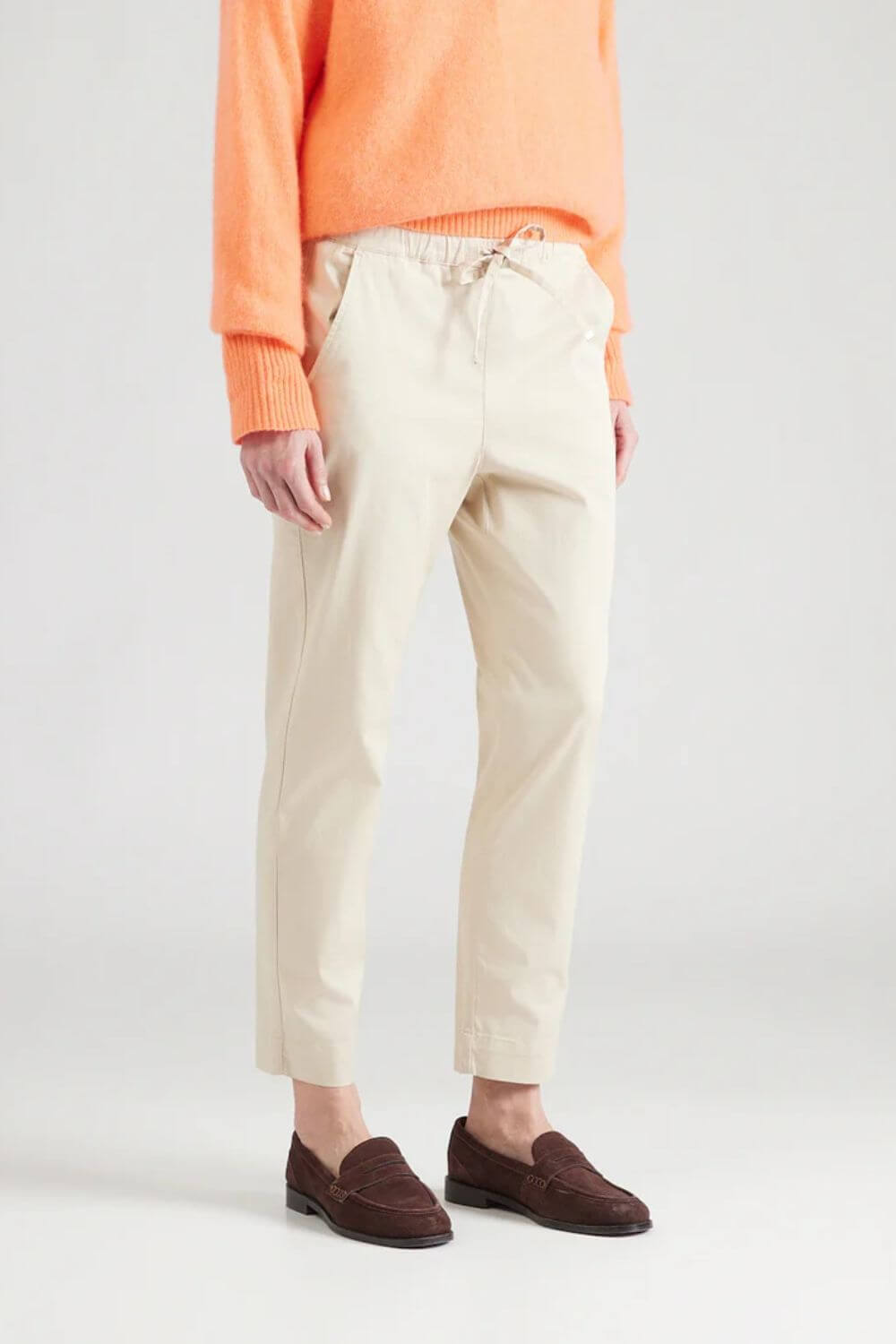 Beige bukser med elastik i livet på model med brune loafers og orange bluse.